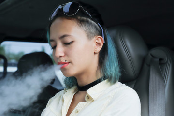 The girl sits behind the wheel in the car and smokes vape. Vap smoke