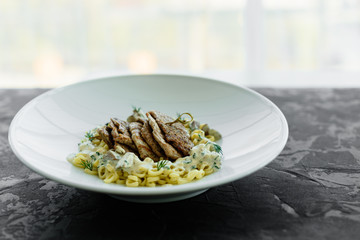 Dish with meat pieces, pasta, greens, sauce from a foie gras and the olive earth