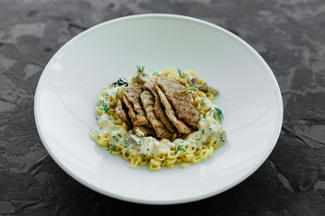 Dish with meat pieces, pasta, greens, sauce from a foie gras and the olive earth