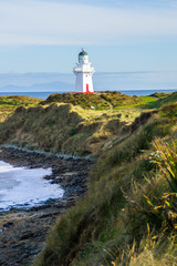 Fototapeta na wymiar Travel New Zealand. Scenic view of white lighthouse on coast, ocean, outdoor background. Popular tourist attraction, Waipapa Point Lighthouse located at Southland, South Island. Travel concept.Catlins
