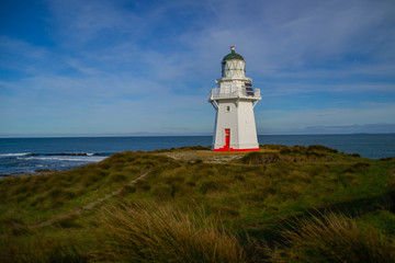 Fototapeta na wymiar Travel New Zealand. Scenic view of white lighthouse on coast, ocean, outdoor background. Popular tourist attraction, Waipapa Point Lighthouse located at Southland, South Island. Travel concept.Catlins