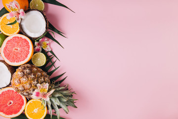 Summer fruits. Tropical palm leaves, pineapple, coconut, grapefruit, orange and lime on pink background. Flat lay, top view, copy space