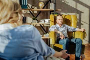 Short-haired old man resting in armchair with a wide smile