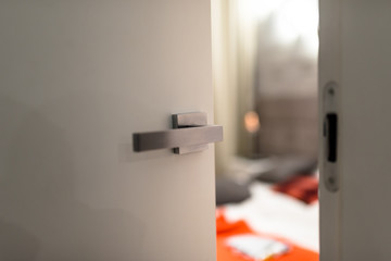  Ajar door to a modern bedroom with a light, visible blurred bed, bedding and orange pillows.