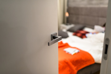  Ajar door to a modern bedroom with a light, visible blurred bed, bedding and orange pillows.