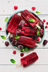 Homemade raspberries blackberry popsicles decorated berries and mint leaves on a white rustic...