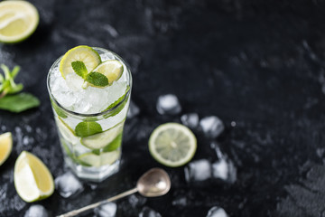 Mojito cocktail with lime and mint in highball glass on a dark stone background. Fresh summer...