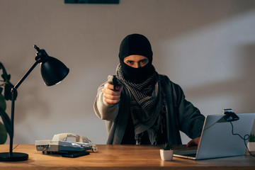 Angry terrorist in black mask aiming gun at camera