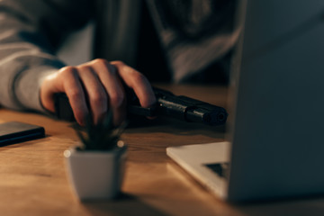 Partial view of terrorist with gun using laptop at table