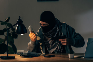 Criminal in black mask holging pistol and looking at handset