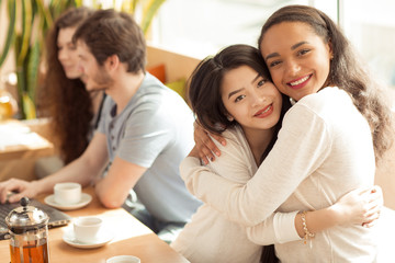 Two beautiful female friends embracing at the cafe