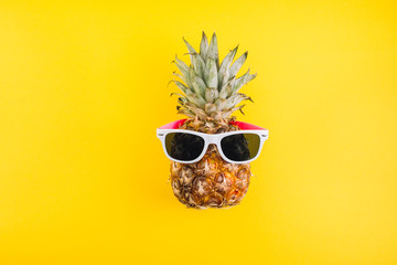 Summer concept. Cute and funny pineapple with sunglasses on yellow background.