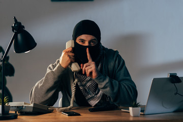 Terrorist in mask talking on telephone and showing hush sign