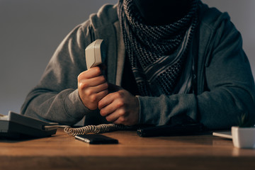 Partial view of terrorist in keffiyeh scarf holding telephone handset