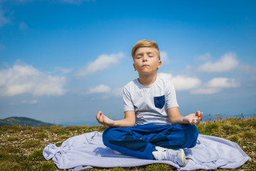 Naklejka na ściany i meble Peaceful boy meditating with eyes closed against the sky.
