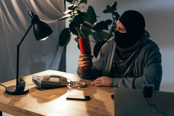 Terrorist in mask sitting in room and holding dynamite