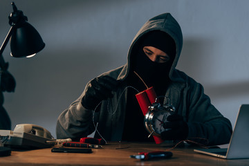 Concentrated terrorist in mask and gloves making bomb in room