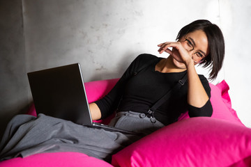 Pretty Asian woman working on laptop while sitting on beanbag chair in office