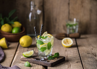 Fototapeta na wymiar Mojito cocktail with lime, lemon and mint in a glass on a dark rustic background. Fresh summer cocktail. Lemon mojito
