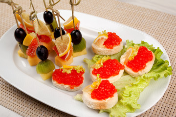 Appetizer with lemon and olives and sandwiches with red caviar on an oval white dish.