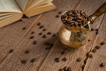 fresh roasted coffe beans in  cezve (traditional turkish coffee pot) opened book and cup on wooden table.