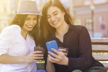 Beautiful girlfriends enjoying coffee using smart phone outdoors