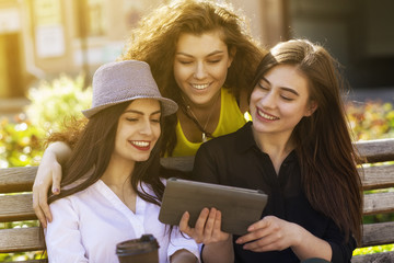 Beautiful girlfriends enjoying coffee using smart phone outdoors