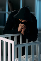 Kidnapper in black hoodie looking in crib and showing please gesture