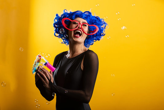Fun woman playing with bubble machine wearing blue wig
