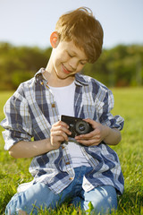 Little boy resting at the park taking pictures with a retro camera