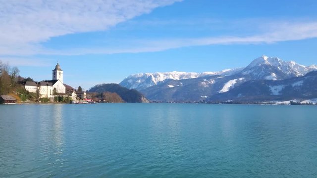 ST WOLFGANG, AUSTRIA - FEBRUARY 23, 2019: Panorama of Wolfgangsee lake with Pilgrimage Church, Strobl town on opposite bank, snowy Alps and ferries in terminal, on February 23 in St Wolfgang.