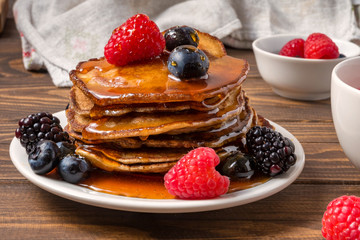 Pancakes covered by honey with blueberries and strawberries on wooden background. Close Up. Soft focus.