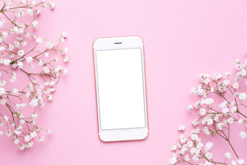 Mobile phone mock up and white flowers on pink pastel table top view in flat lay style. Woman working desk.