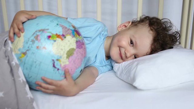 the kid, the boy in the crib, pretends to sleep with the globe in his hands. Emotions, smile, laughter.