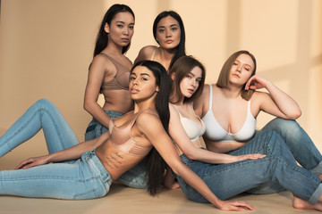 five dreamy multicultural young women sitting in sunlight and looking at camera, body positivity concept