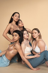 five multicultural women in blue jeans and bras looking at camera, body positivity concept