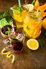 Refreshing summer berry Lemonade, lemon mint Tea and orange Lemonade with rosemary on wooden table in rustic style. Copy space.