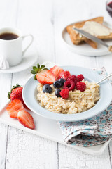 Oatmeal porridge with fresh blueberries, raspberries, muesli and almonds in red bowl on white table. Healthy breakfast, healthy eating, vegan food concept. Colorful breakfast for kids