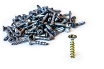 golden modern screw screwed into a white surface on the background of the heap of gray used screws