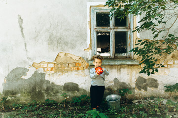 beautiful boy with a white hair red mug and a bucket on the background of the old hut