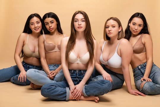 five beautiful multicultural girls in blue jeans and bras sitting and looking at camera, body positivity concept