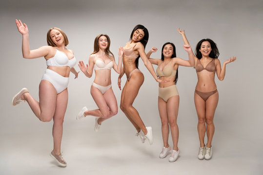 five attractive multicultural young women in lingerie having fun and jumping, body positivity concept