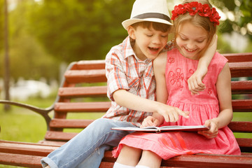 Happy kids reading a book together outdoors