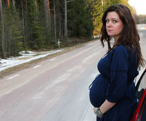 A pregnant woman by a car on a road