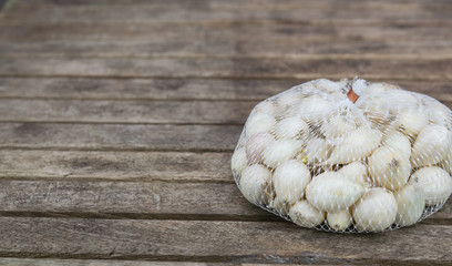 Farming,cultivation, agriculture and vegetables concept: small white onion in a plastic netting bags,prepared for planting in the garden on a wooden table.
