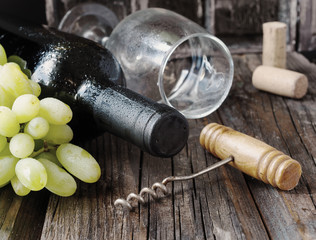 Bottle of red wine with fresh grape and bunch of corks on wooden table