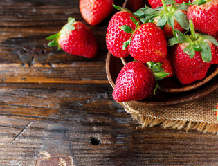 red ripe strawberry in a wooden bowl on a rustic table, selective focus