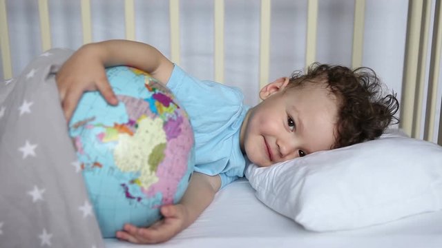 the child, the boy in the crib, does not want to sleep, plays with the globe, the ball.