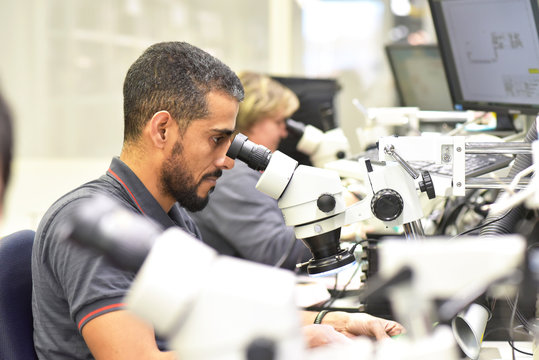 Man using a microscope for the quality control in the manufacturing of circuit boards for the electronics industry
