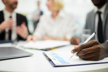 Closeup of African businessman signing document during meeting in office, copy space